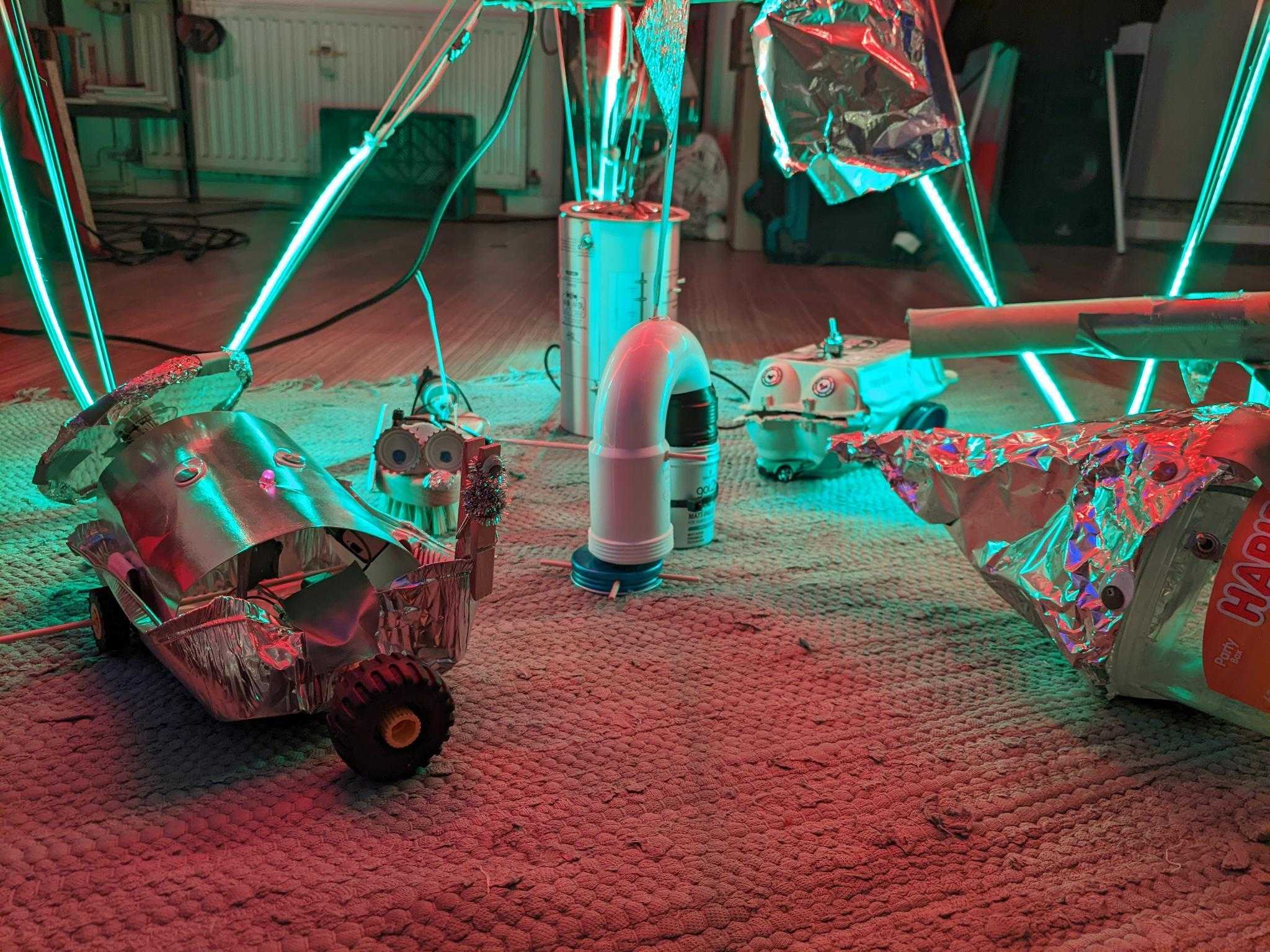 Selbstgebastelte Roboter auf einem Teppich in neonfarbener Beleuchtung